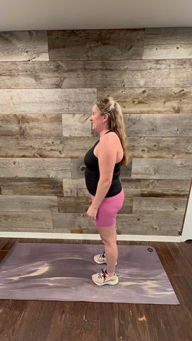 A person in pink shorts and black tank top standing on a mat