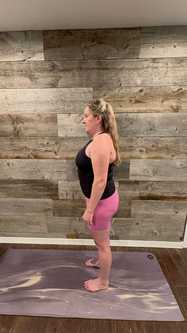 A person in pink shorts and black tank top standing barefoot on yoga mat