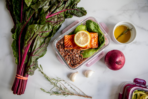 Cooked salmon meal prepared in glass dish with fresh spinach and wild rice with red onion, garlic and bunch of swiss chard on counter